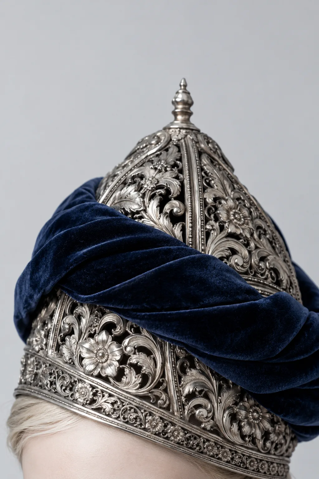 Close detail of an ornate silver filigree helmet wrapped in navy velvet